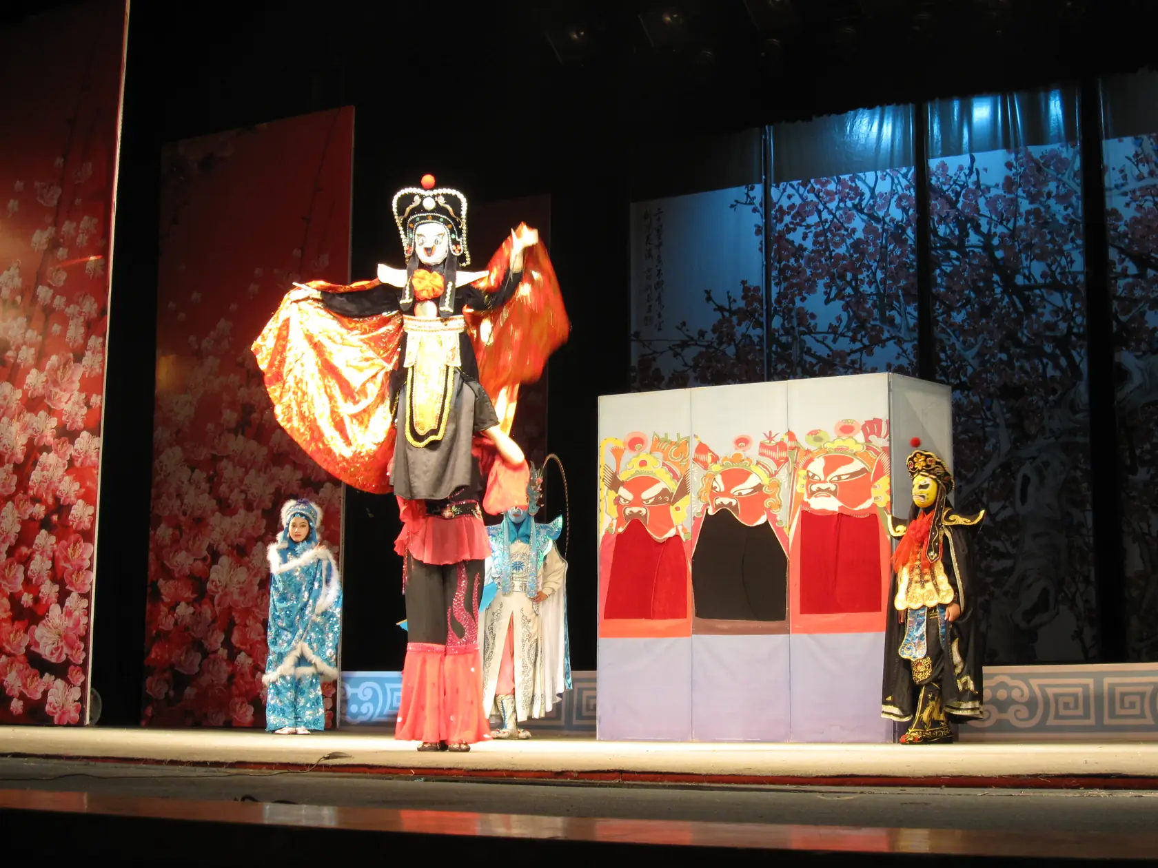 Sichuan opera performers on stage in ornate costumes and painted masks